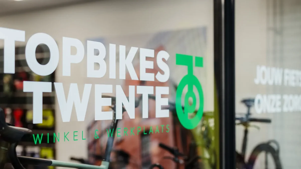 Voorkant van het raam bij Topbikes Twente, fietsenwinkel in Oldenzaal. Op het raam staat een sticker met logo van Topbikes Twente.